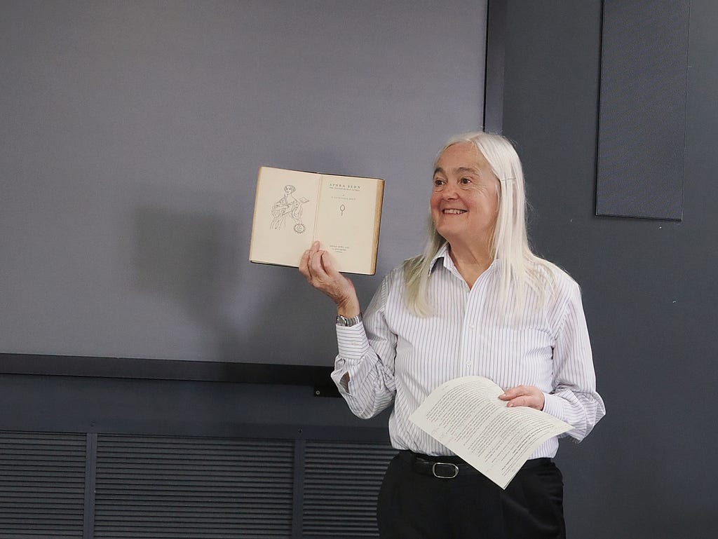 Professor Emerita Elaine Hobby holding up a novel by Aphra Behn during a lecture.