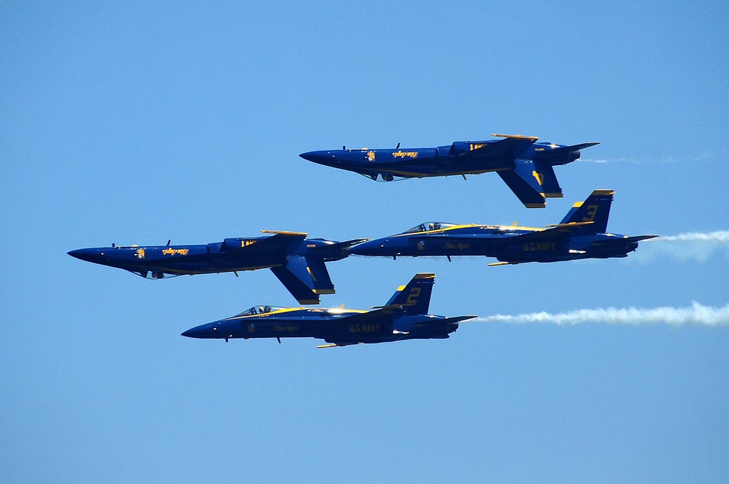 Four blue milltary jets in a tight acrobatic formation