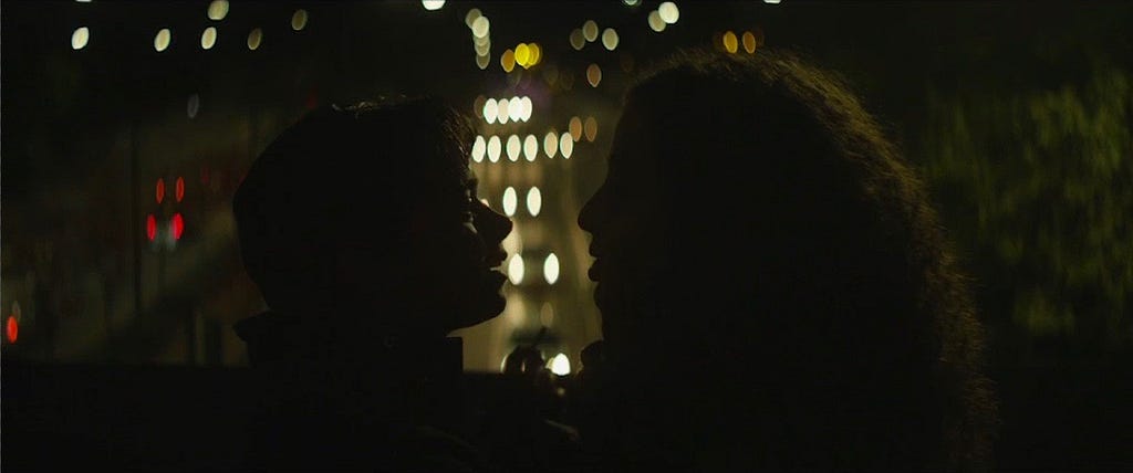two young people facing each other in silouette at night, street lights can be seen behing them