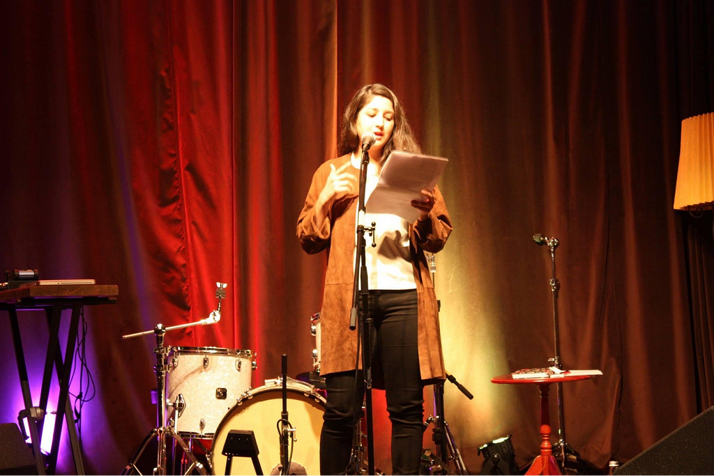 Michelle en escena recitando un poema, rodeada de tambores, micrófonos y un teclado