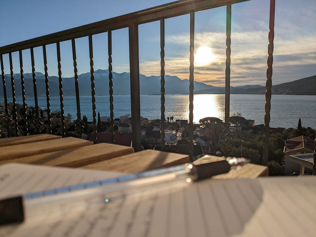 A view of the sunrise over the bay of Kotor from our apartment balcony. A journal and writing pen rest in the foreground.