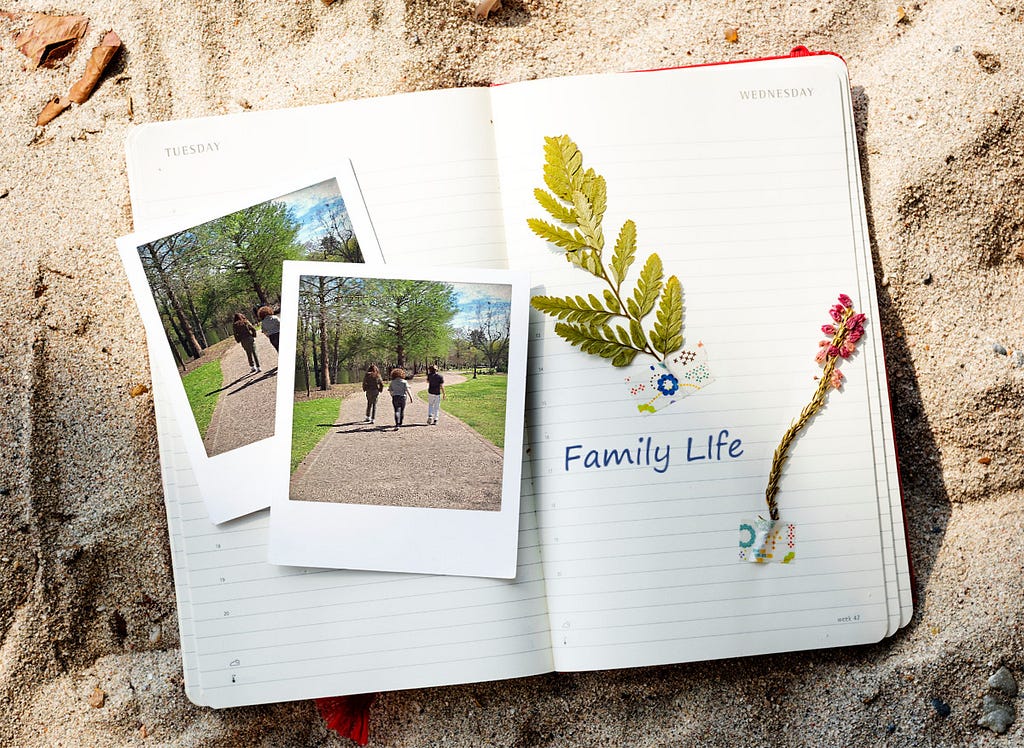 An open diary on sand showing two Polaroid photos of a family and a child riding shoulders, with ‘Family Life’ written alongside leaf and flower decorations.