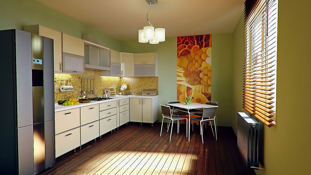 Kitchen with sunlight showing through the blinds. There’s a table with four chairs, a painting in the back, a large refrigerator on the left, and the kitchen counter and cabinets to the right of the refrigerator. Wooden plank floor.