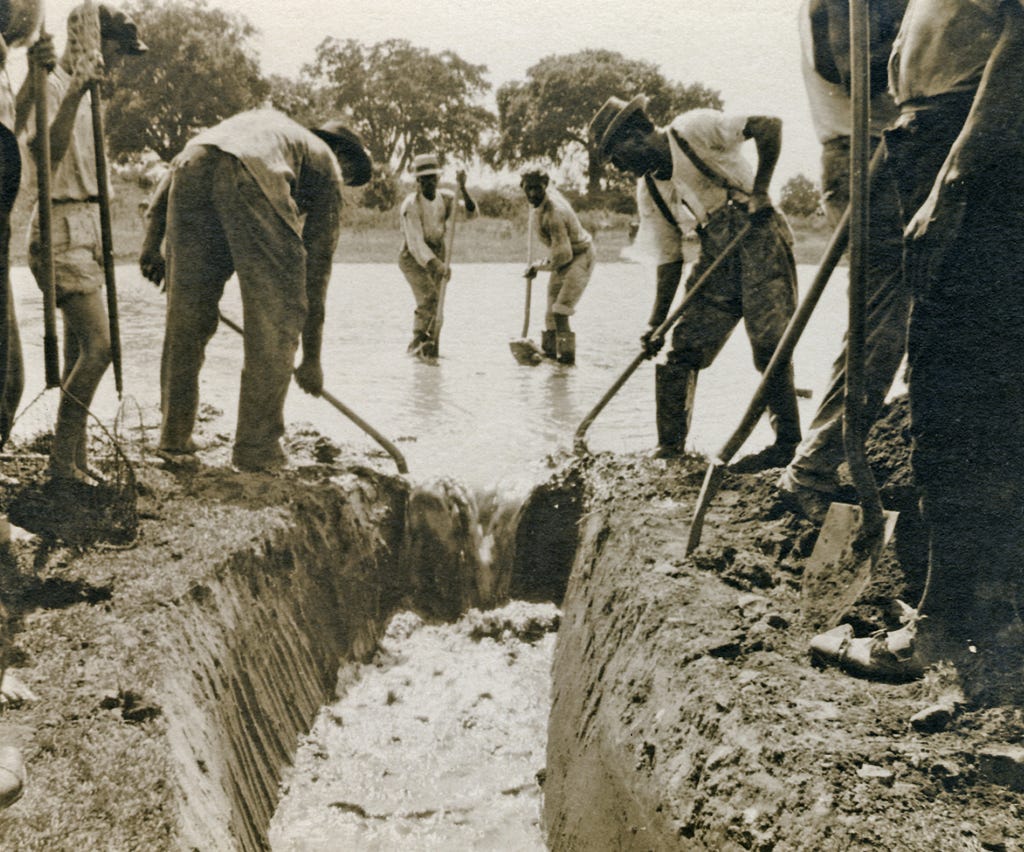 An old photograph depicting several men working in a muddy pit filled with water.