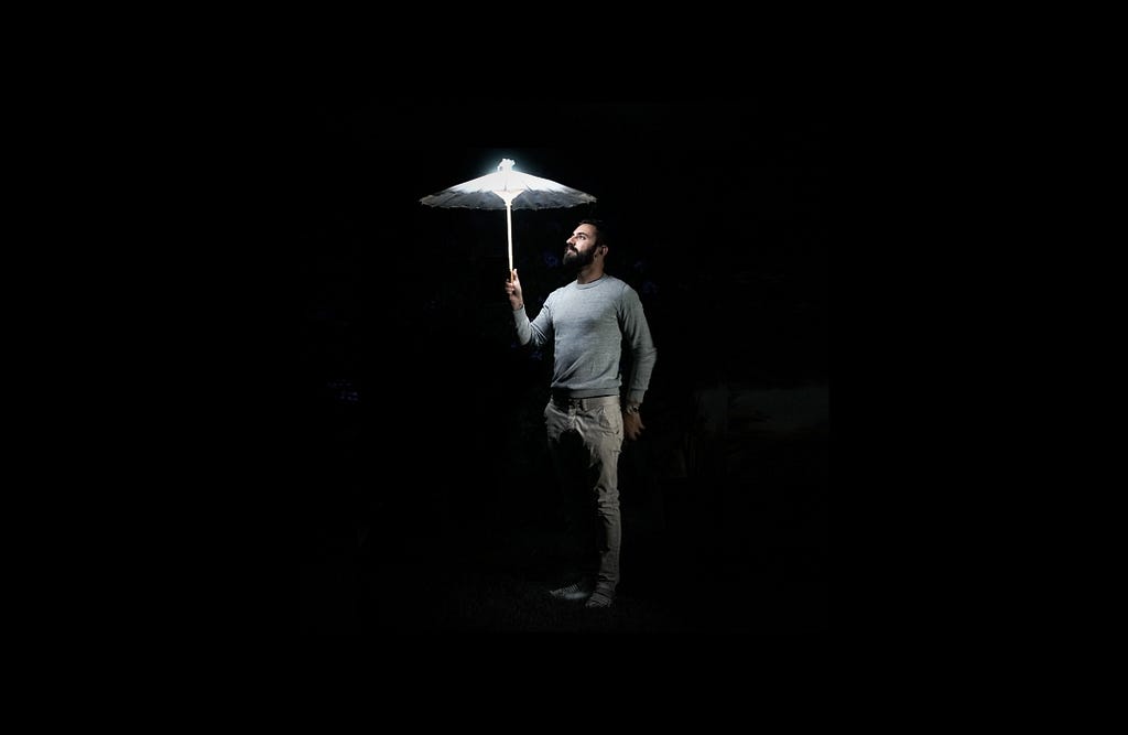 A man holding a glowing, light-giving umbrella in a dark environment.