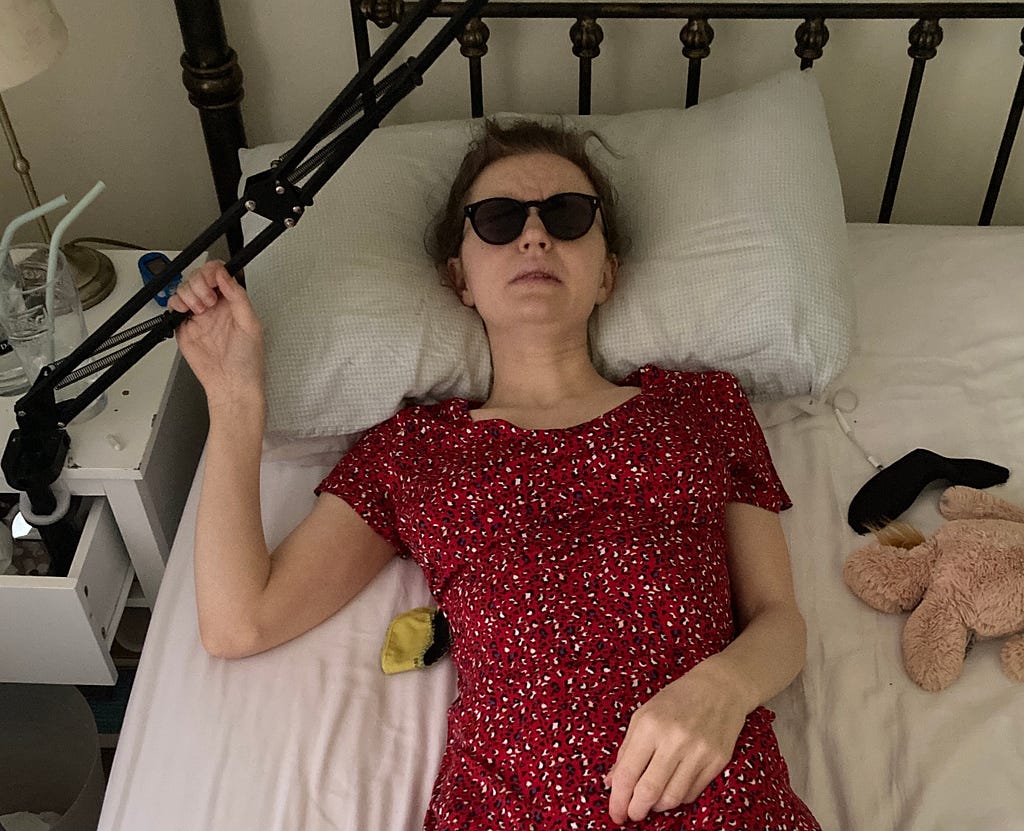 Sophia lying in bed with dark glasses holding on to her phone holder
