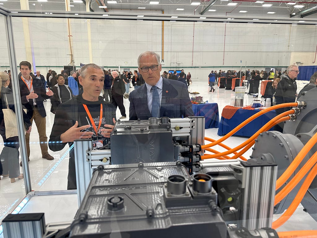 Photo of two people looking at an aircraft component with orange wires in a glass case