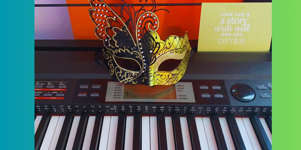 The image of a white and black medeli piano that belongs to the author. The author’s signature mask is also sitting on top of the piano with gold and black accents. There is a green sign in the background that says your life is a story write well edit often.