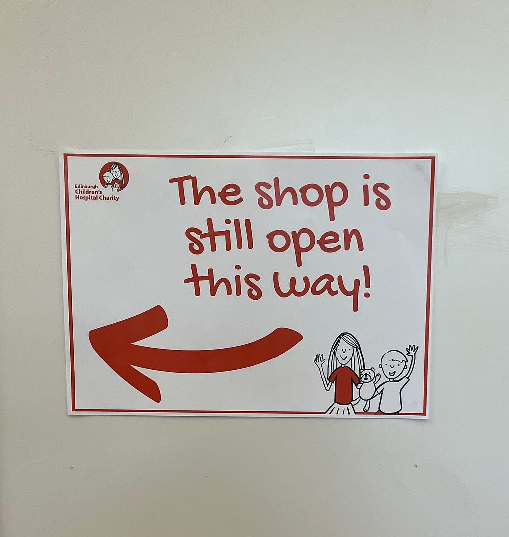 A sign reads “the shop is still open this way” with an arrow and a drawing of 2 children waving