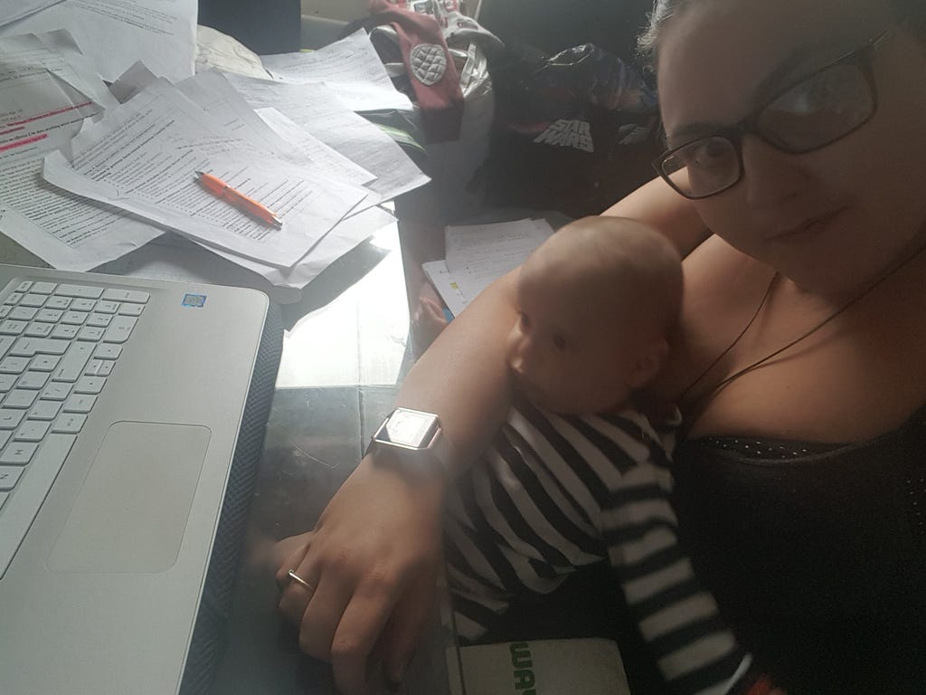 A ‘selfie’ image of Emily studying on a laptop at home, with her baby son sat on her lap.