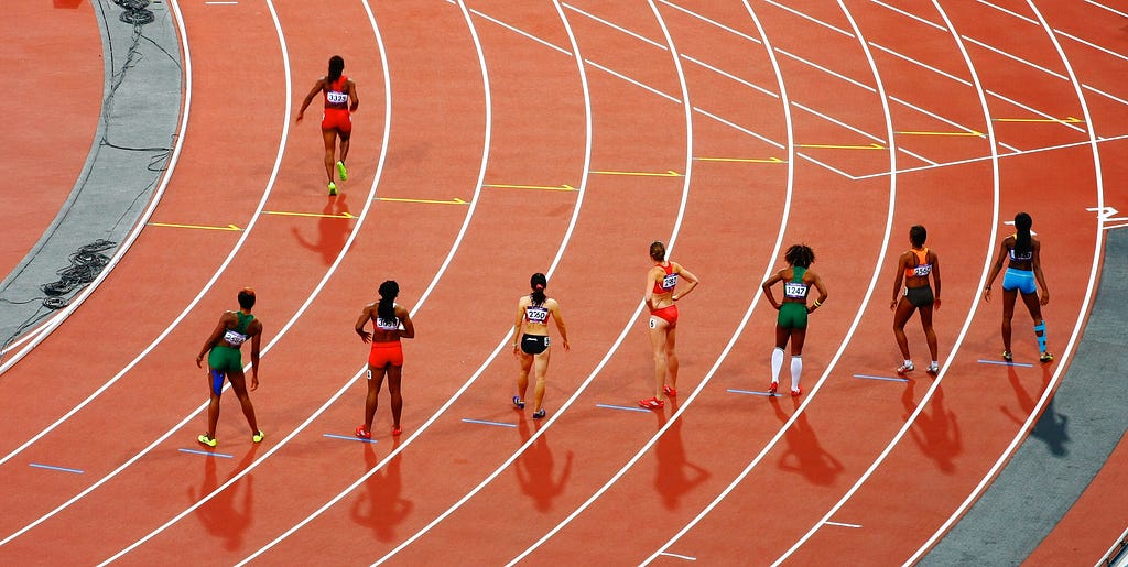 7 women line up to race on a formal athletics running track.