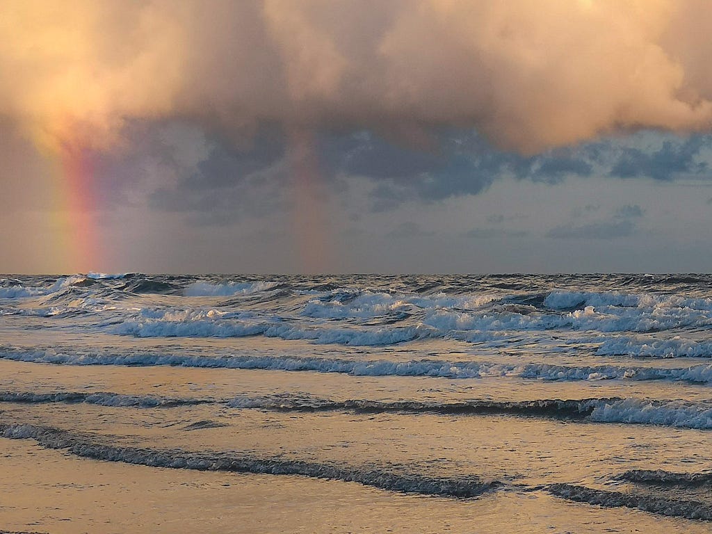 Cloud breaks, rainbow still there over frothy waves