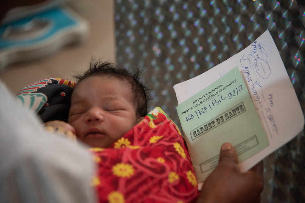 A sleeping infant is held alongside a health book held by its mother.