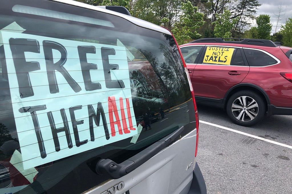 Two cars with signs. One says free them all and the other says justice not jails