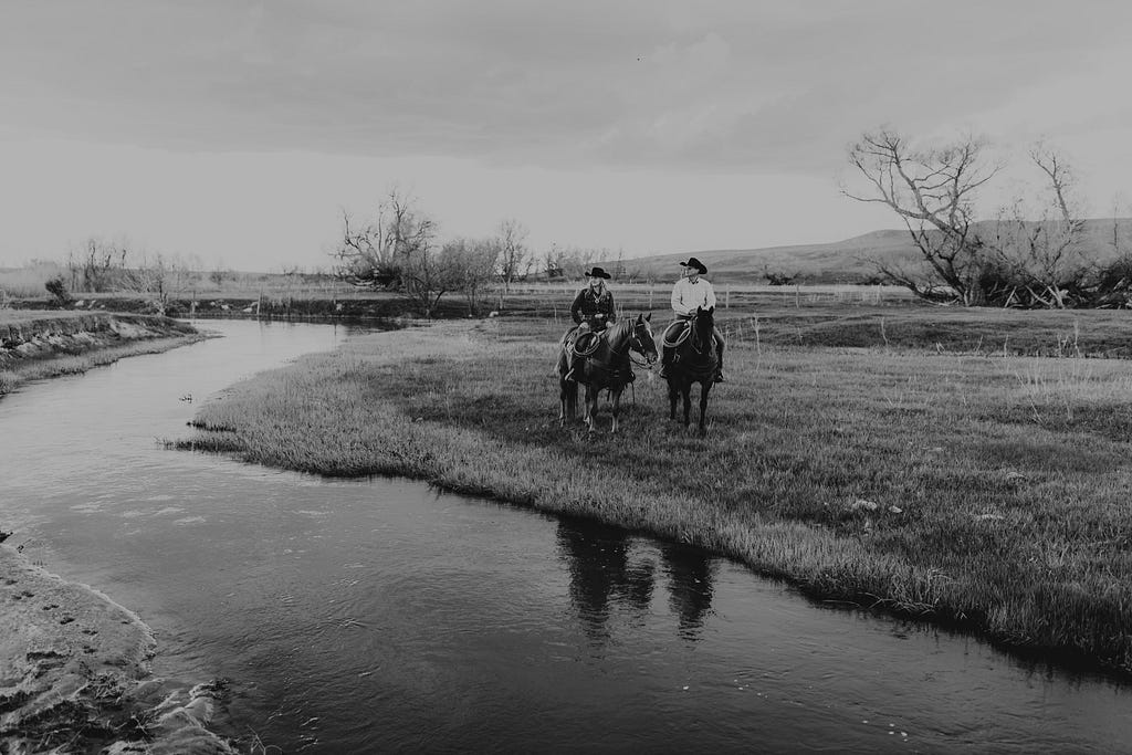 woman and man on horses beside a creek
