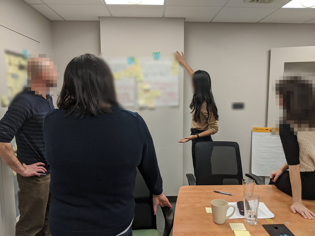 Four people standing around a poster with yellow sticky post-it notes. They are discussing ideas written on the poster.