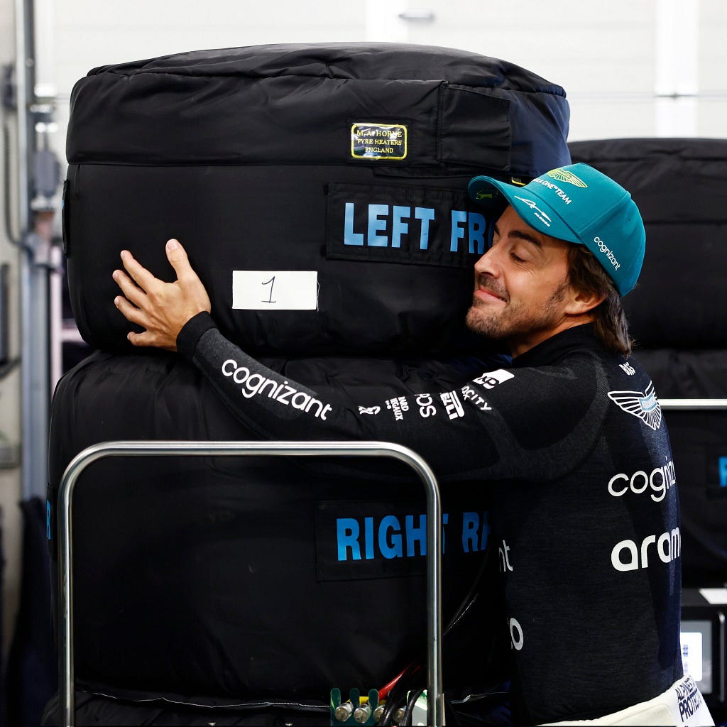 Fernando Alonso is literally hugging a stack of tyres in their tyre blankets and he’s grinning like a dork.