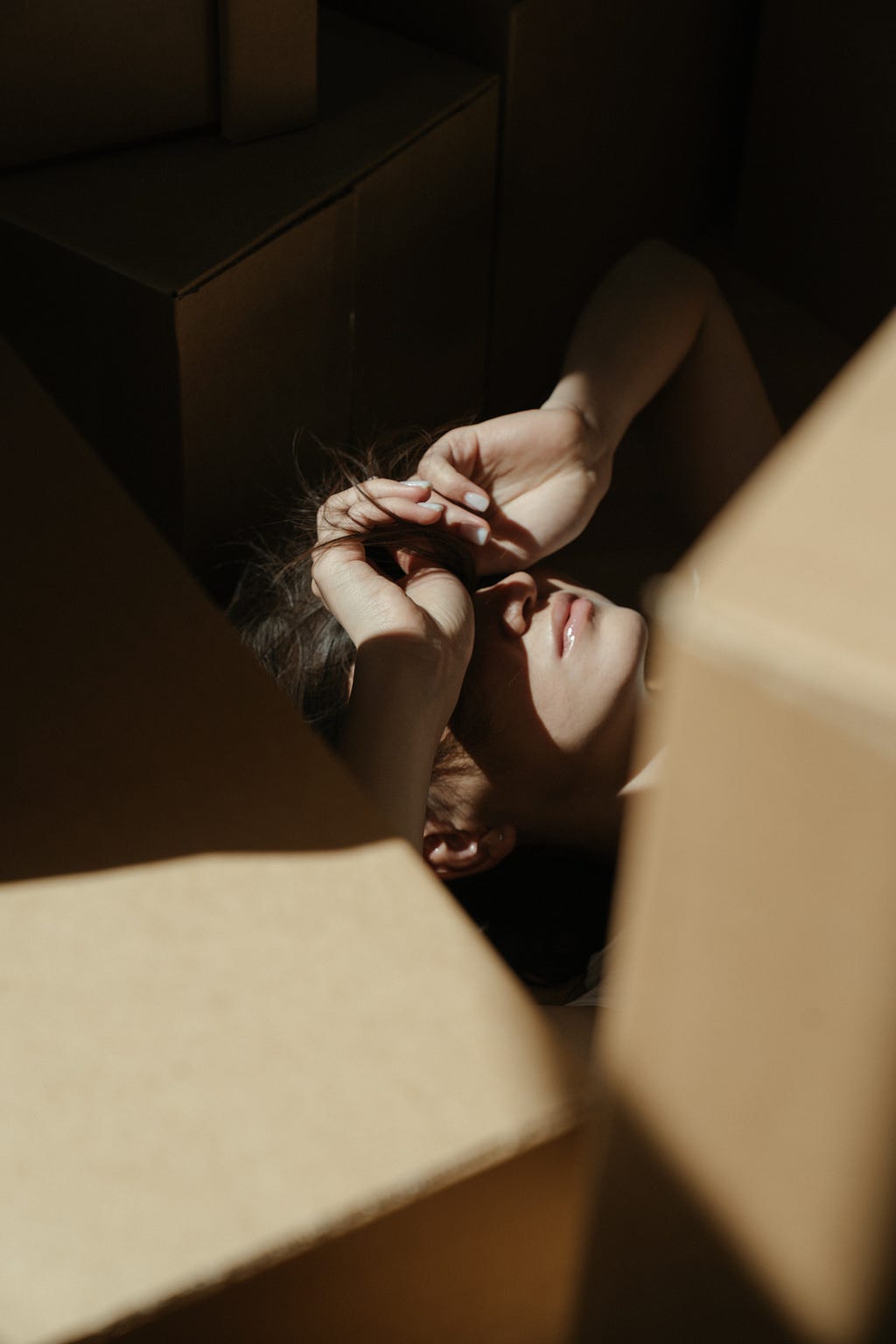 A woman lying on the floor with her hands covering her eyes in distress. There are multiple boxes around her.