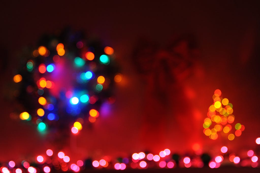 Blurred holiday lights in multi-color with red-tinged sky.