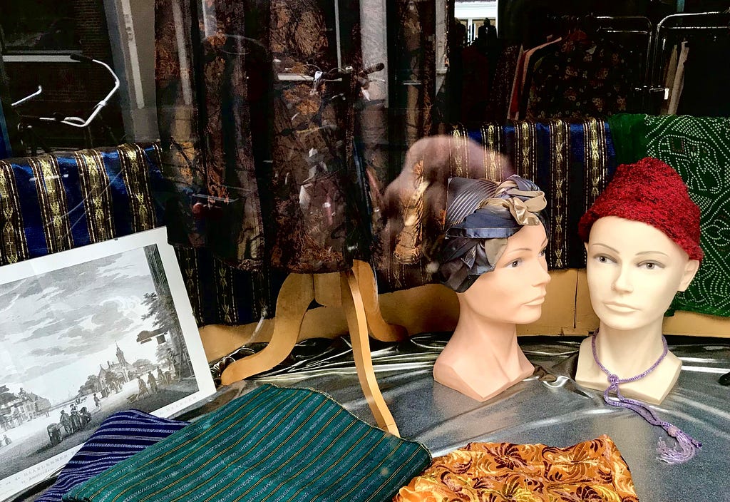 A shop window that displays fabrics and two sculpted heads wearing a headscarf and knitted hat.