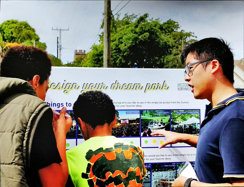 Ryan speaking to two youth in front of a display board, which reads “Design your dream park”