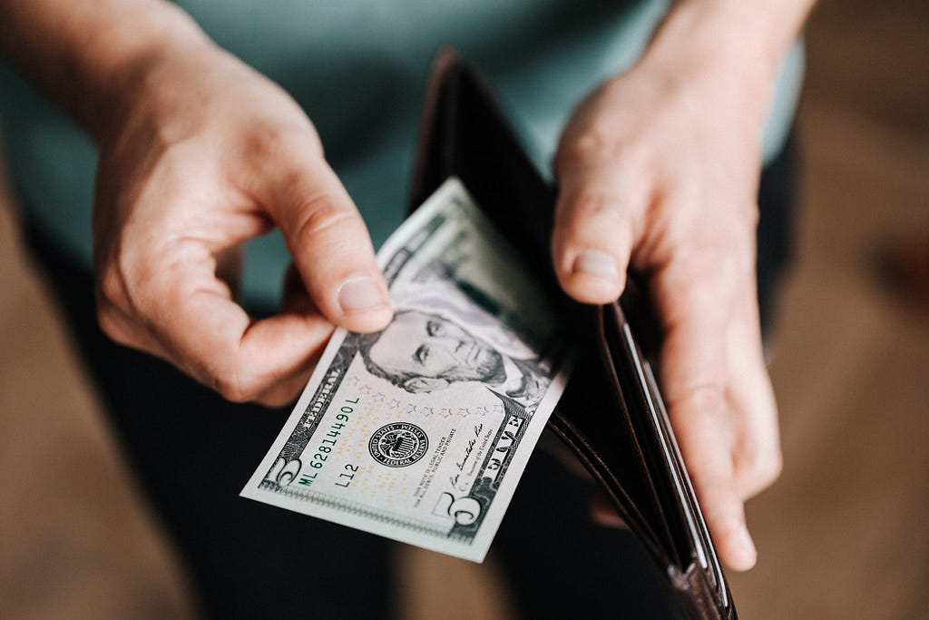 Man holding an open wallet with a five dollar bill