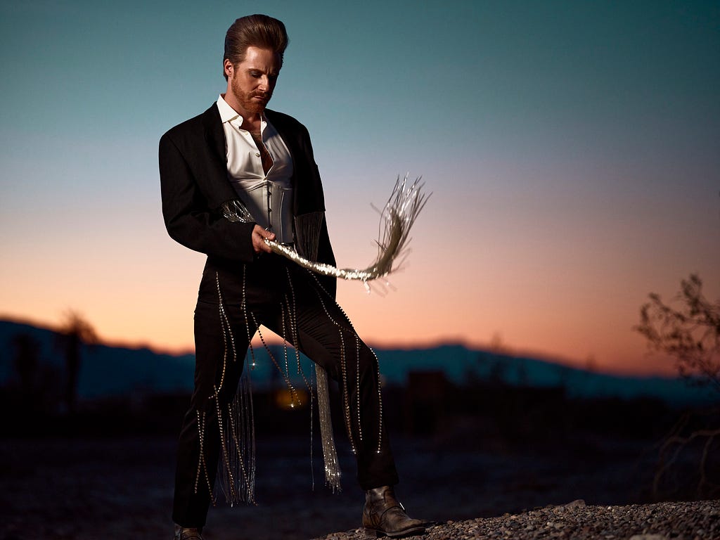 Fashionable man with silver whip standing in desert at dusk