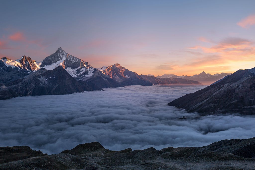 Clouds floating in a valley between snowy mountains.