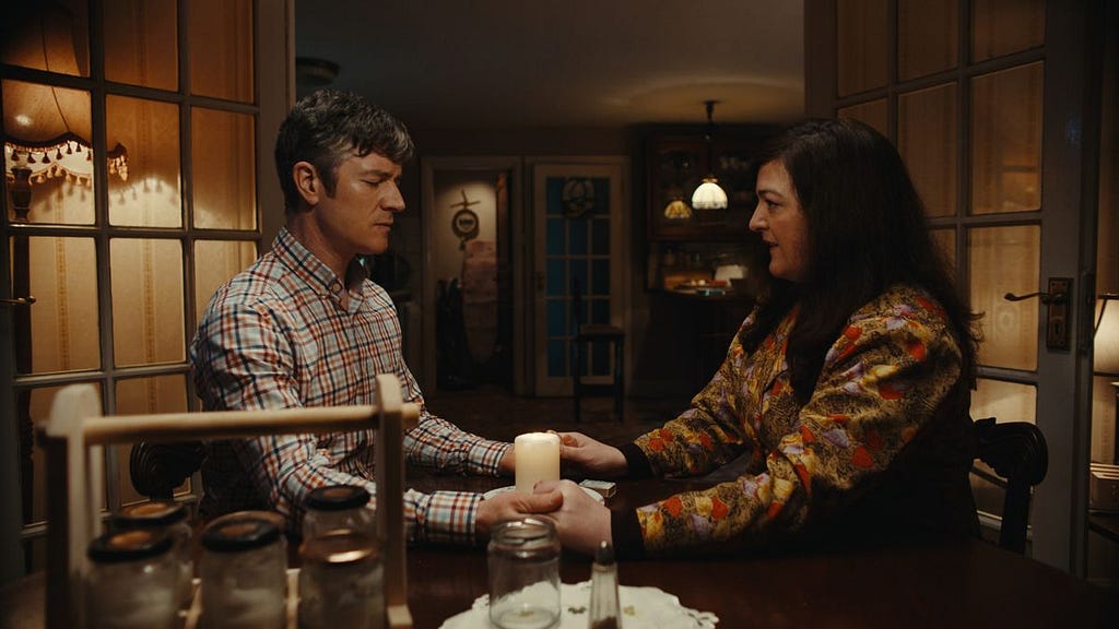 frame from extra ordinary showing martin and rose holding hands as rose performs a spell in martin’s kitchen