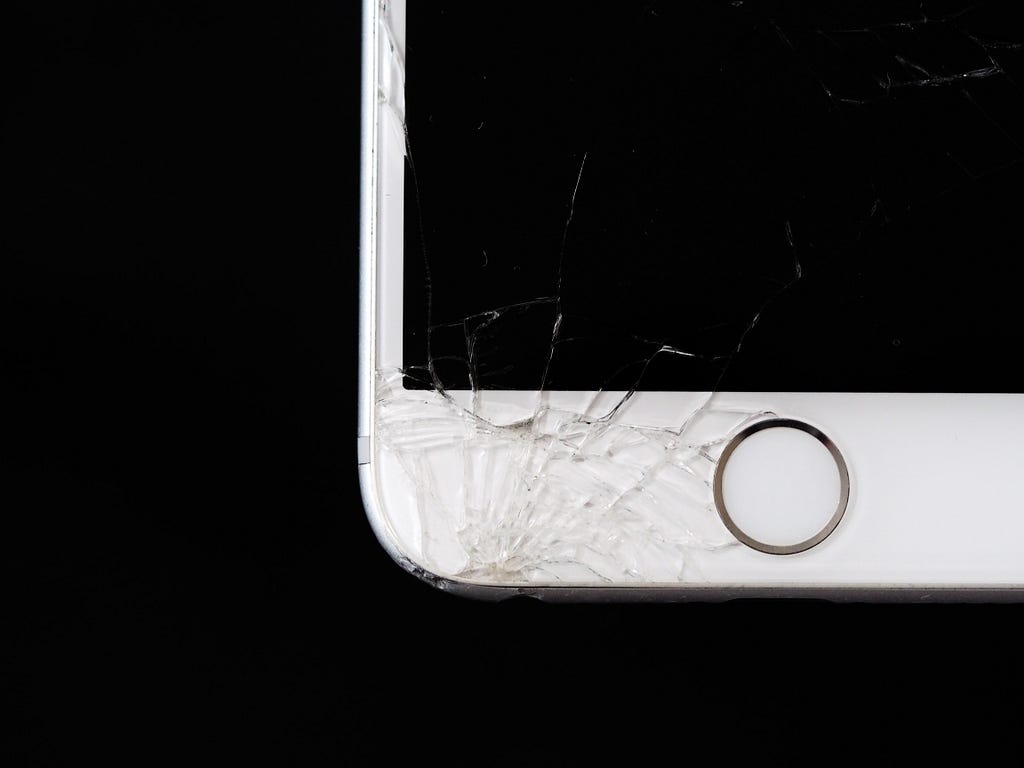 A cracked Iphone, the crack being on the bottom left of the phone’s front.