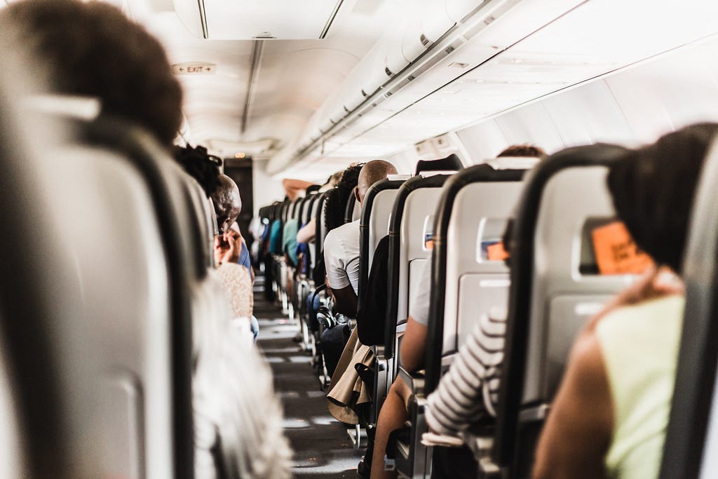 View from the back toward the front of a plane interior, with people seated in the rows ahead.