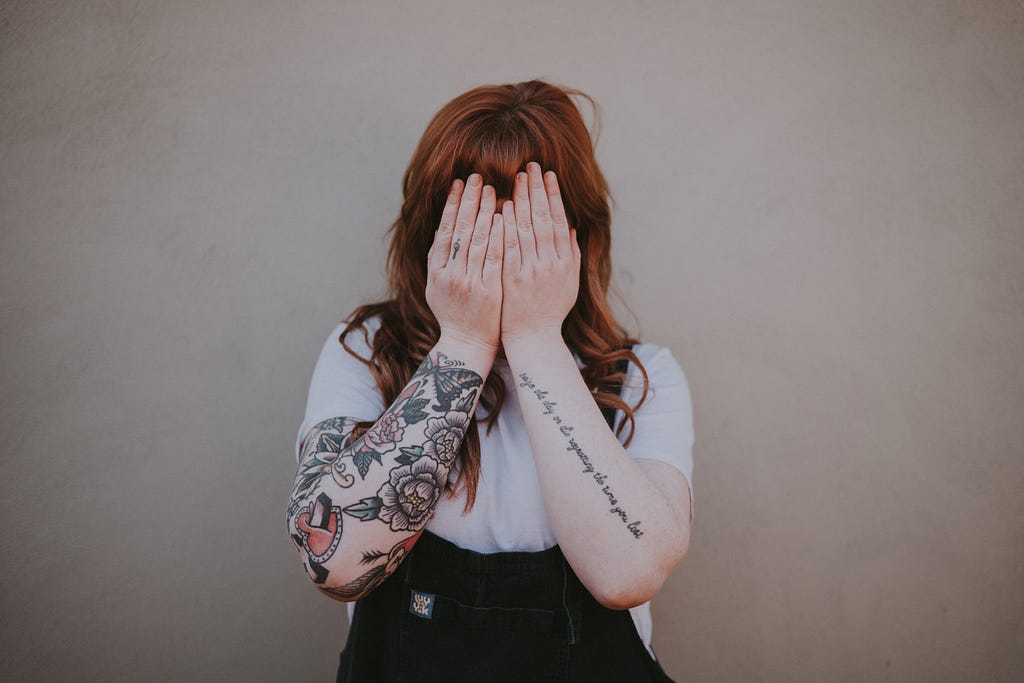 Tattooed woman covering her face with her hands