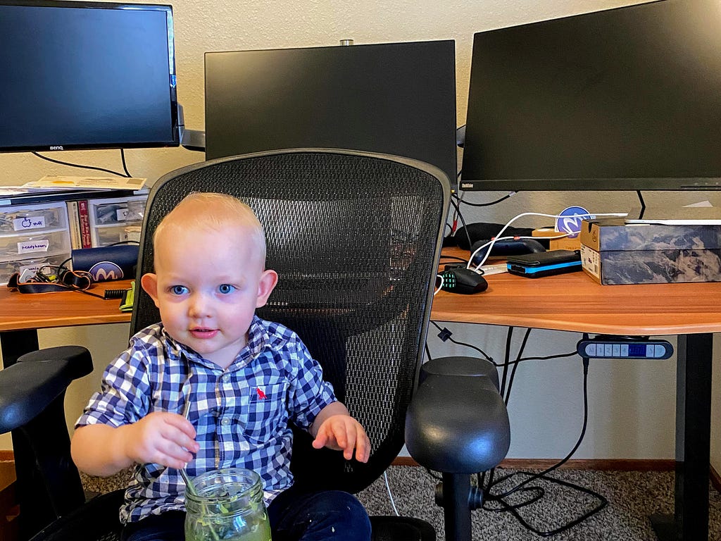 My son Clark sitting in my desk chair in front of my remote work setup.