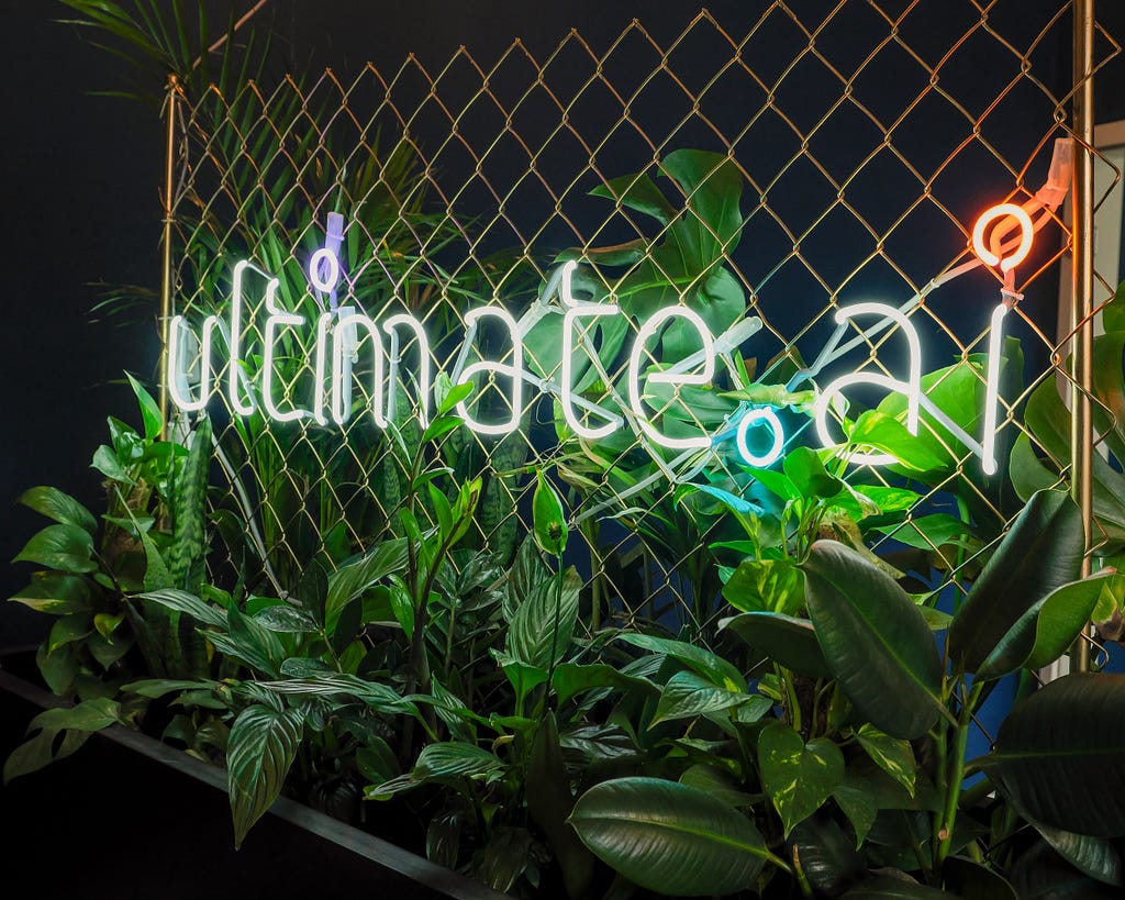 A neon sign of ultimate.ai surrounded by greenery.