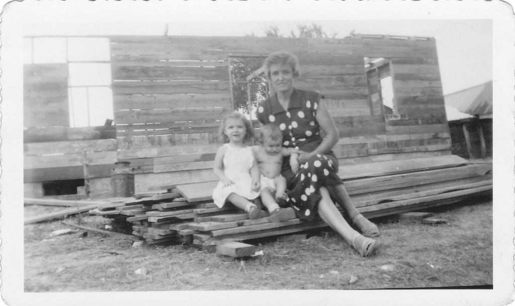 Grandma with grandkids, sitting on building materials for her farmhouse.