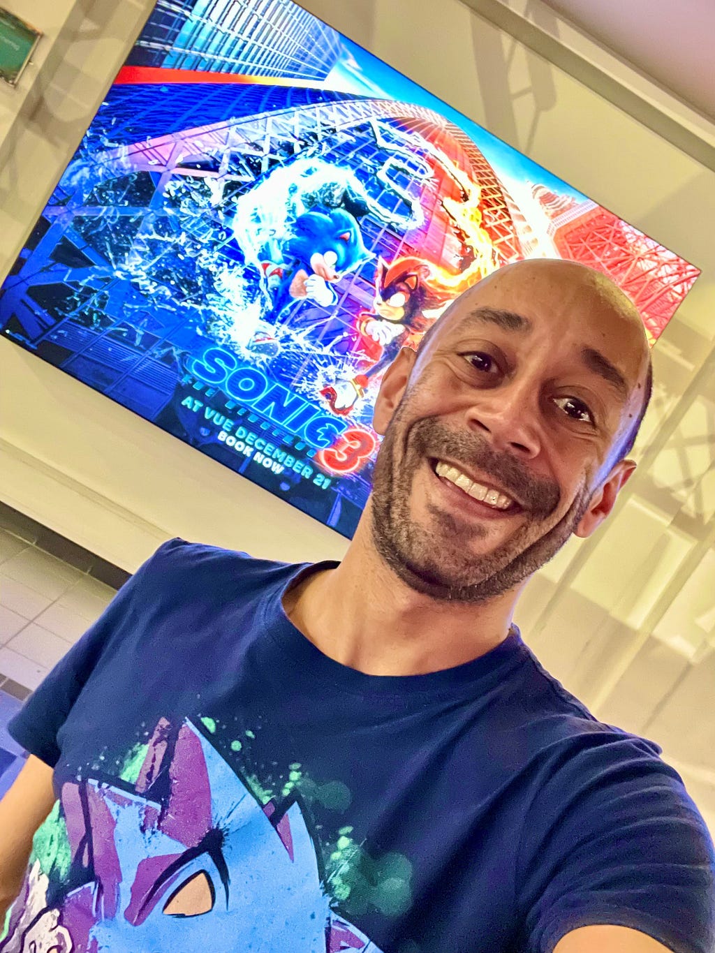 Ant Babajee wears a Sonic the Hedgehog T-shirt and stands in front of a poster for Sonic the Hedgehog 3