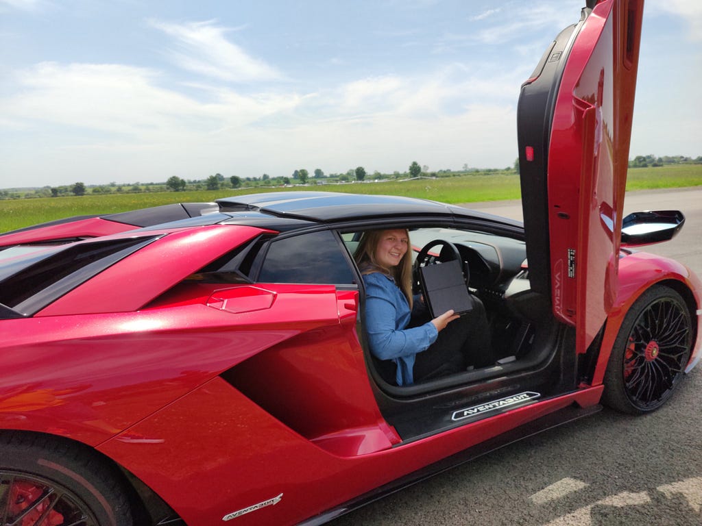 Sophie sitting in a Lamborghini holding the OnePlus Nord CE box.