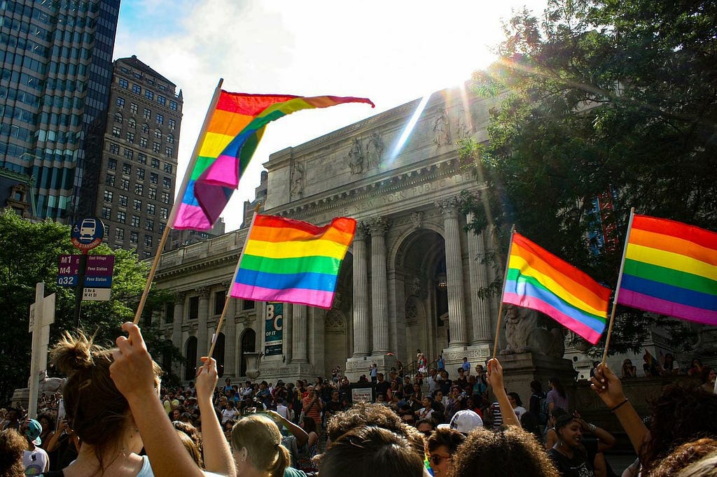 A crowd waves Pride flags in front of a government building.
