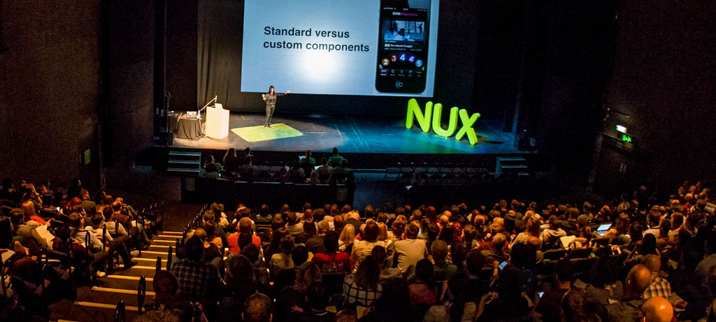 Women on stage giving a presentation about design system components to an auditorium full of people.