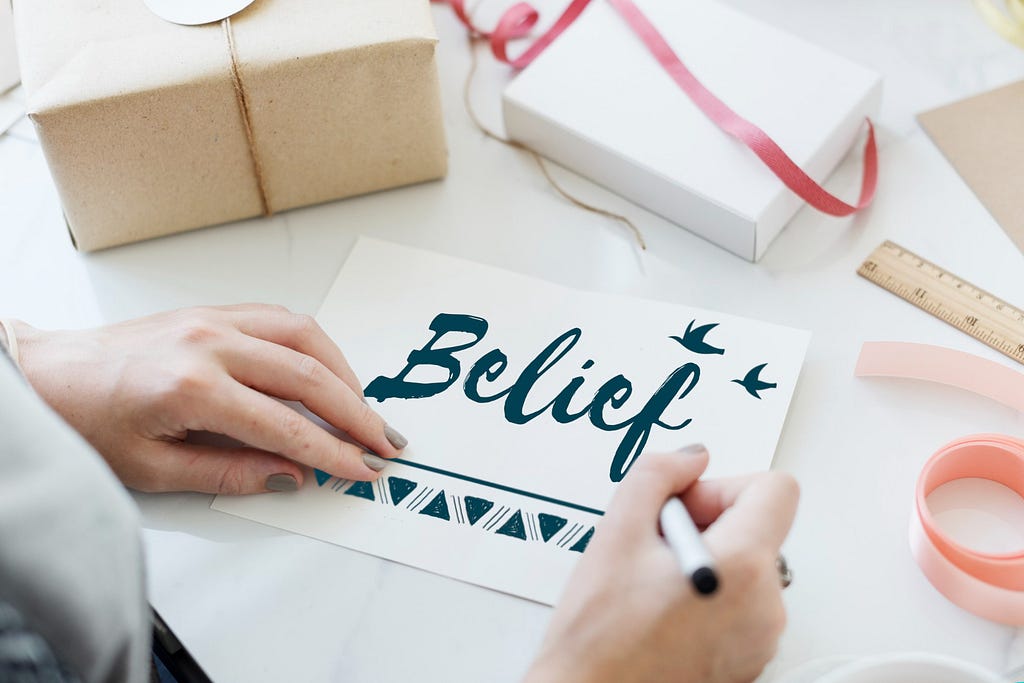 An Woman Writing belief on a white glossy paper.