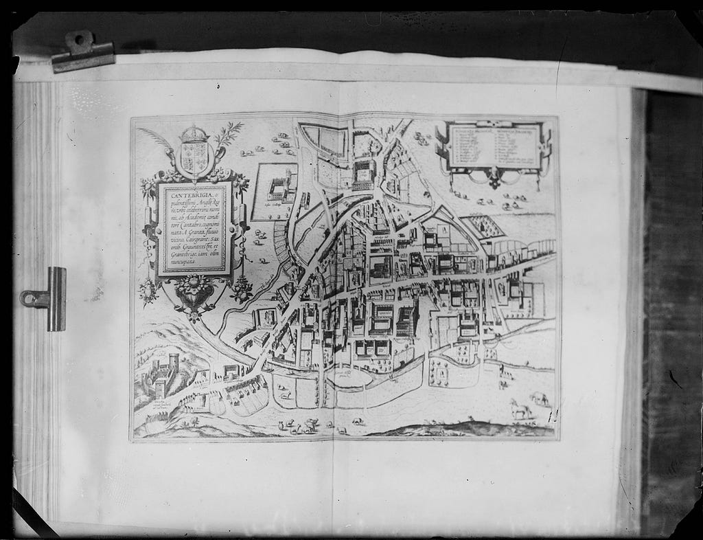 A digitised and inverted glass plate showing a book with a map of Cambridge held open by bulldog clips