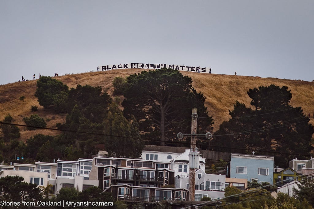 A banner spells out “Black Health Matters” on top of a hill in San Francisco. Text: Stories from Oakland | @ryansincamera.