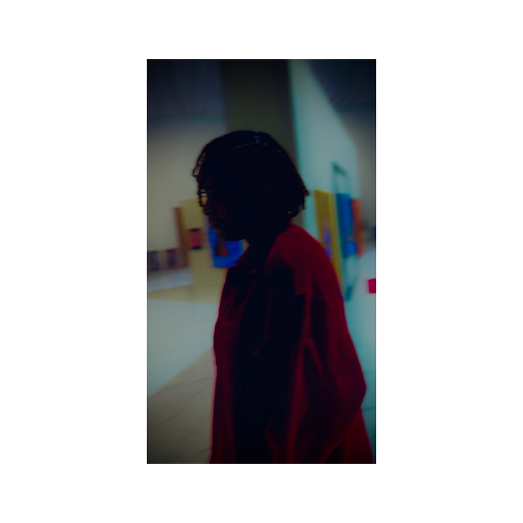 A picture of the Author, Keyukemi at art exhibition. The picture has been edited to highlight her red jacket amidst the darkness around