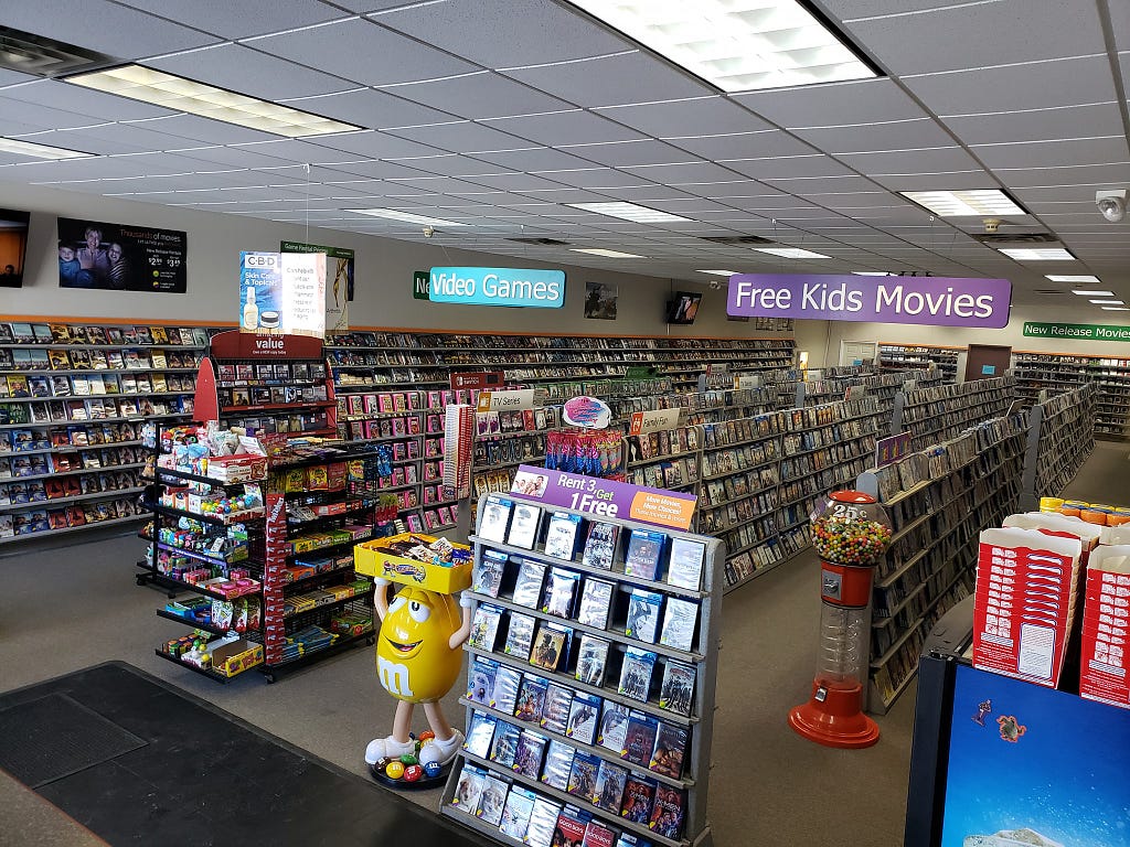 A movie store lined with rows of movies and categories on the walls, candy in the aisles, etc.