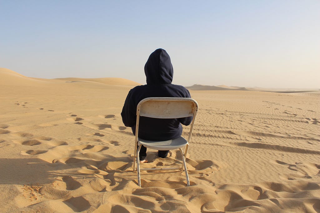 A man sitting in a foldable chair in the middle of the desert