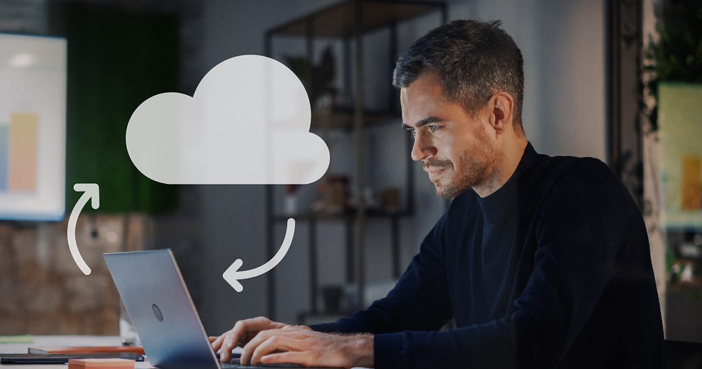Man in black shirt typing on a laptop with a cloud icon hovering above the laptop