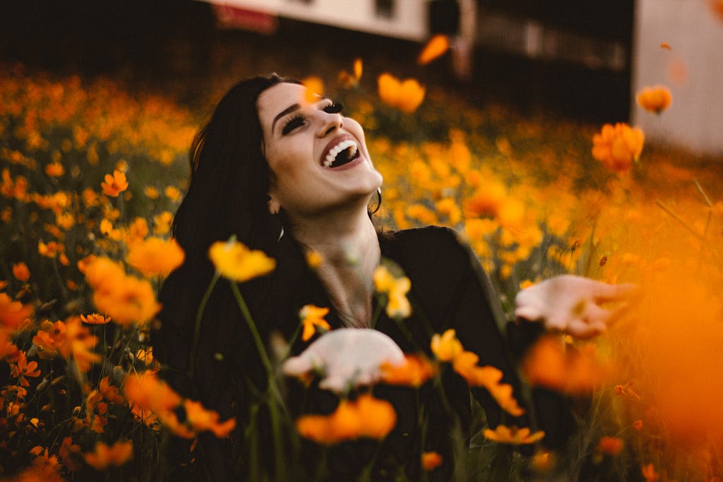 A woman sitting and smiling in the midst of yellow coloured flowers