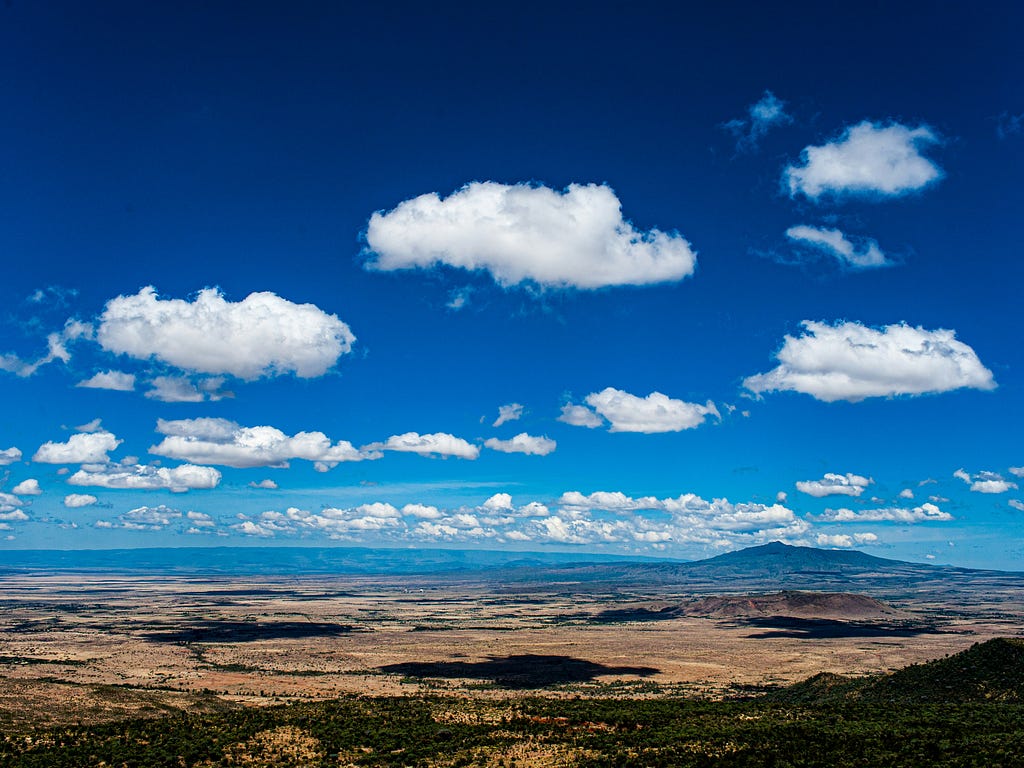 A panoramic view of Mount Longonot, with blue skies in the background and farmlands in the foreground.