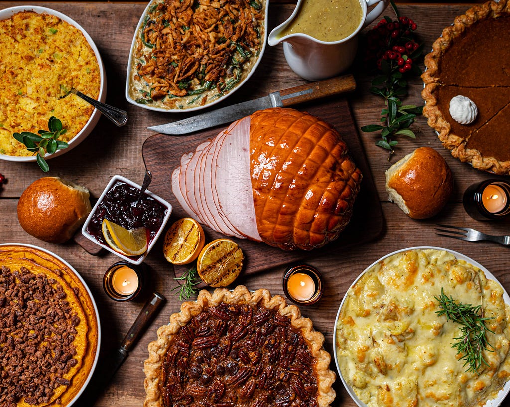 A Thanksgiving banquet complete with sliced ham, green bean casserole, and pecan and pumpkin pies!