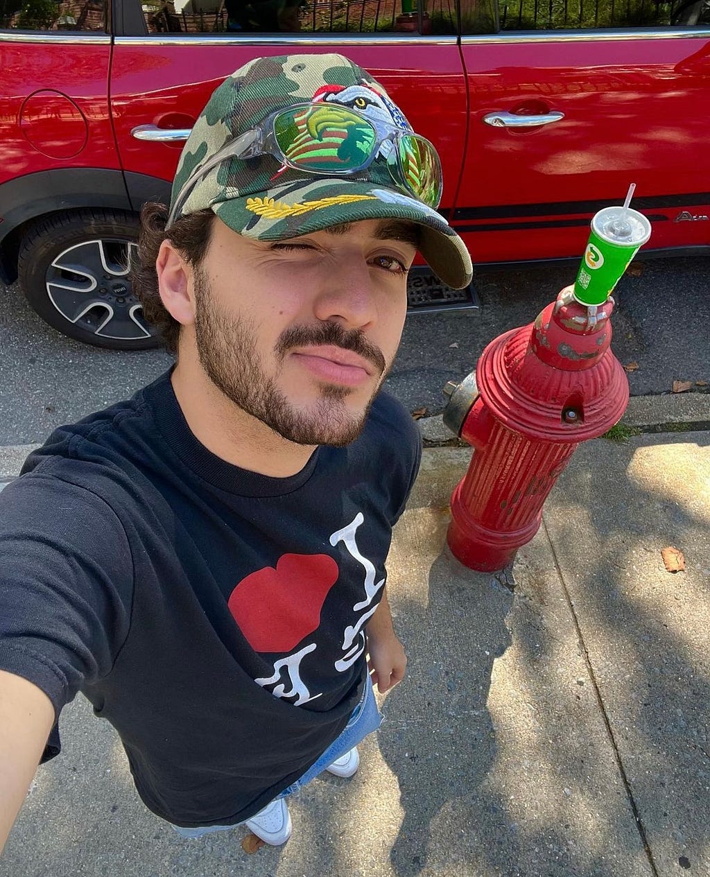 Photo of Alessandro De La Torre squinting at the camera. He is on the street, with a red fire hydrant behind him.